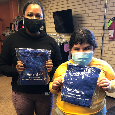 (Click to Read) Photo of an ICONI Team Member and a volunteer holding shirts from the Clothes to Kids of Denver donation