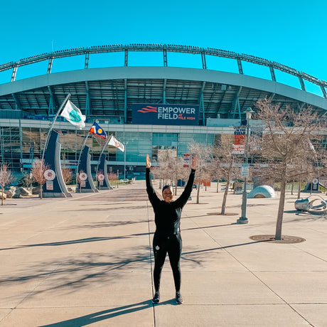 (Click to read) ICONI CEO standing in front of Empower Field, Home of the Denver Broncos, holding hands and arms up in the shape of a touchdown sign