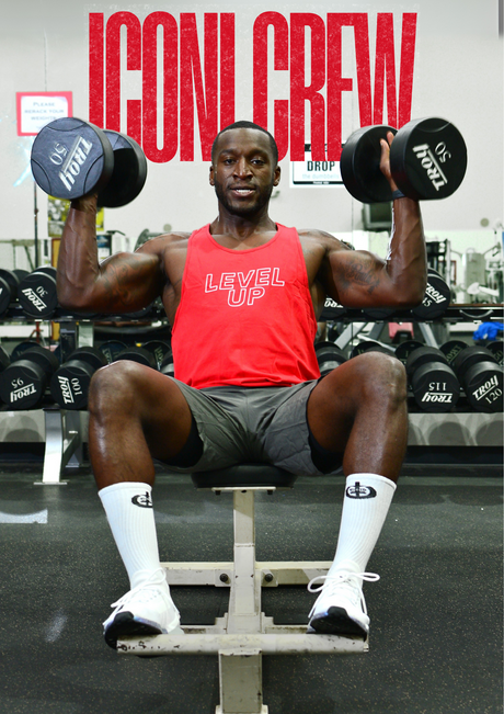 Photo of man lifting weights in a red ICONI tank and gray ICONI shorts with the words ICONI Crew behind him